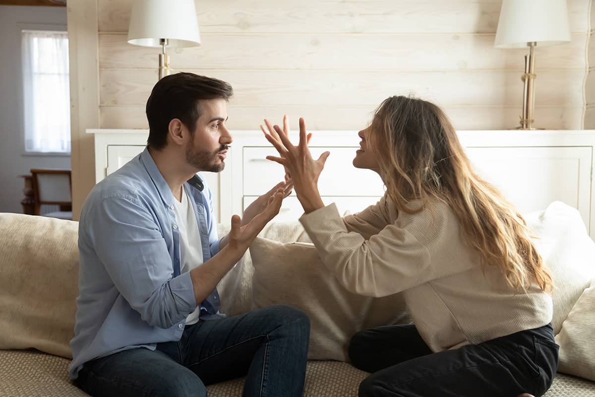 Emotional annoyed stressed couple sitting on couch, arguing at home. Angry irritated nervous woman man shouting at each other, figuring out relations, feeling outraged, relationship problems concept.