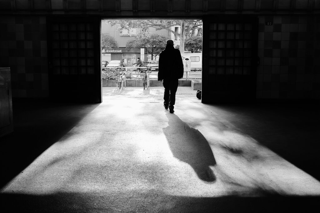 Man walking toward light through dark doorway, representing illness and identity transformation